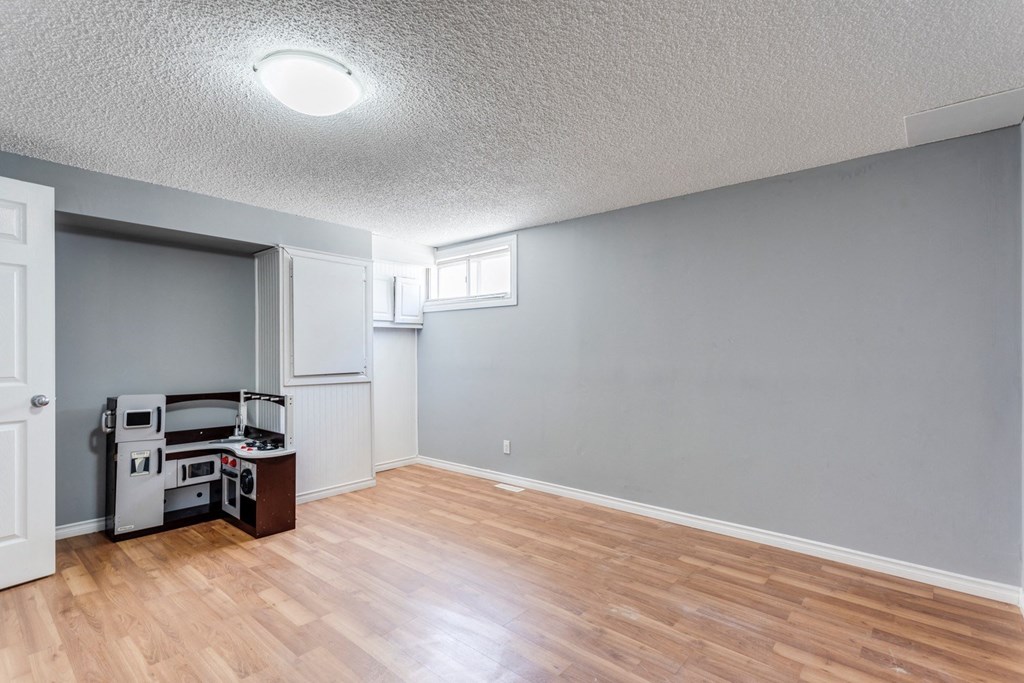 an empty living room with wood flooring and a kitchen with a stove