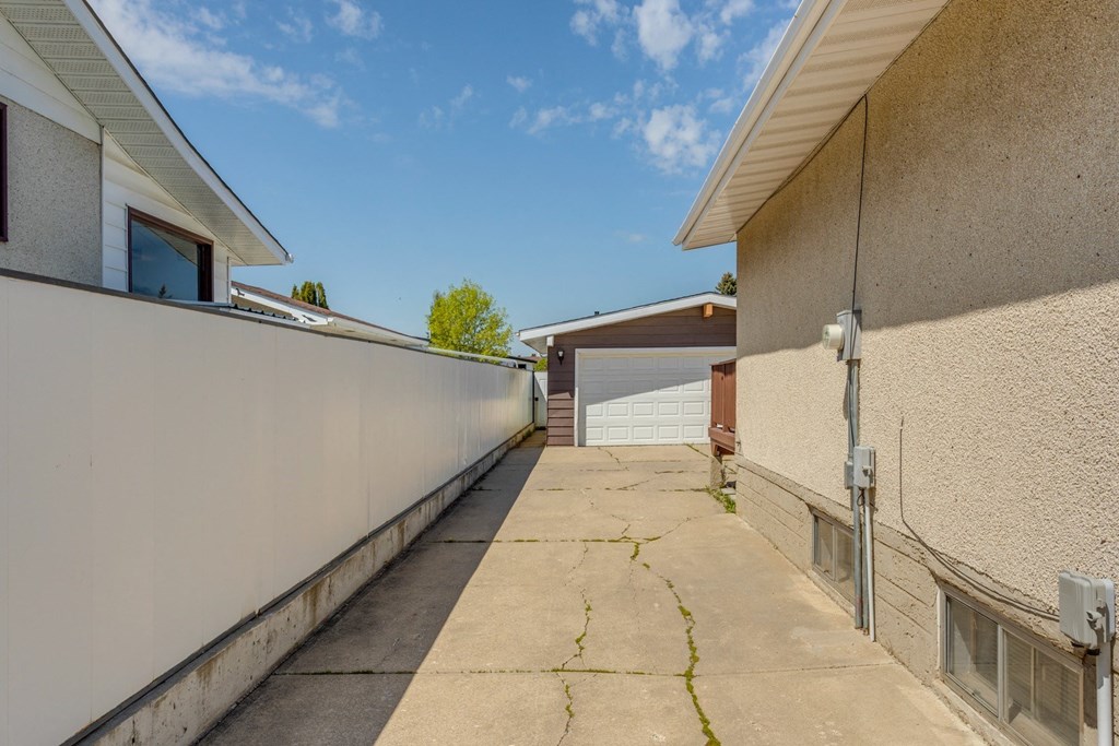 the driveway of a house with a white wall and a concrete sidewalk