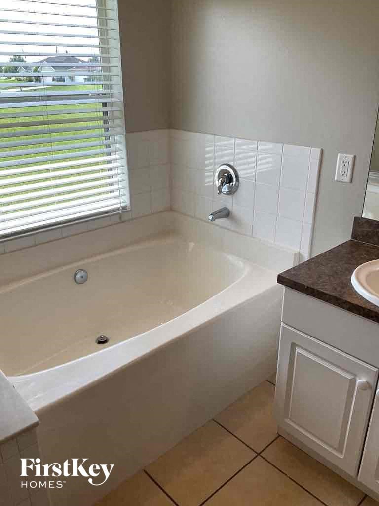 A white bathtub with a brown countertop and a window with blinds.