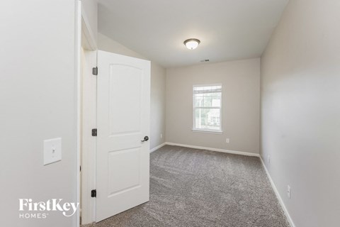 a bedroom with a white door and carpeted flooring and a window
