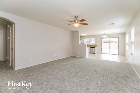 an empty living room with a ceiling fan and a kitchen