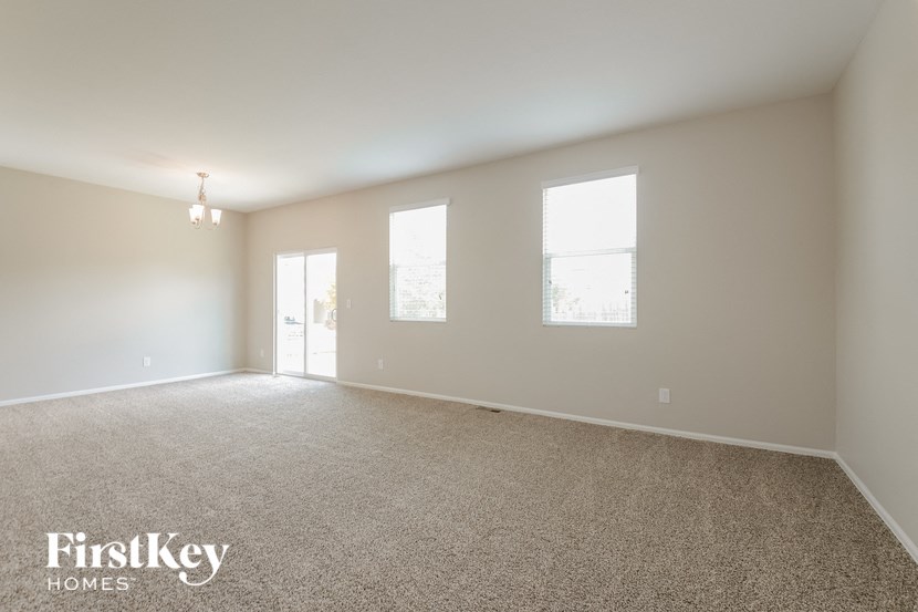 A spacious room with carpeted floor and three windows.