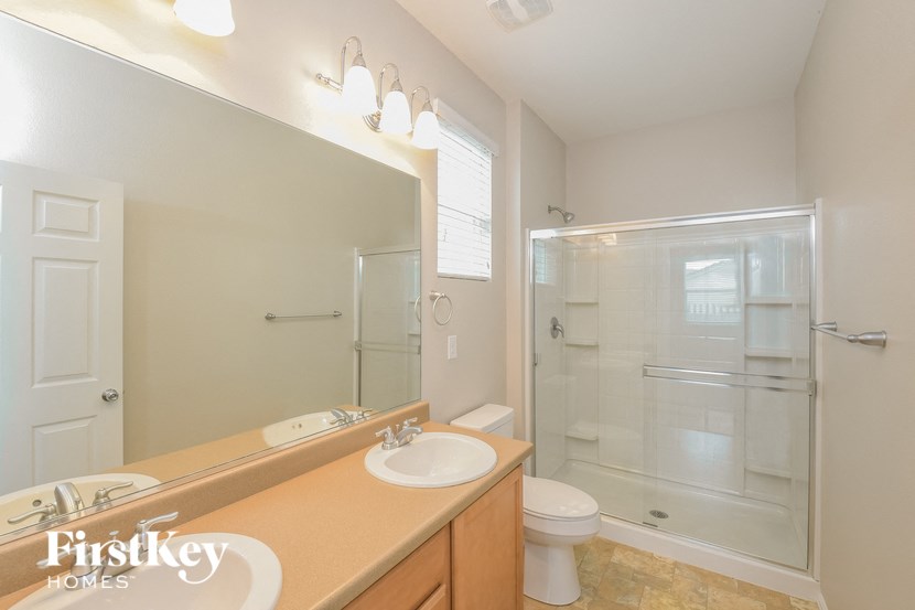 A bathroom with a tan counter top and a glass shower stall.