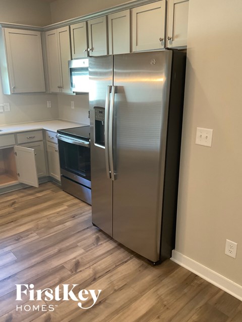 A stainless steel refrigerator in a kitchen with wooden flooring.