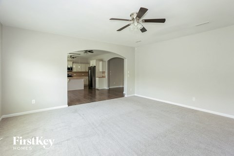 an empty living room with white carpet and a ceiling fan