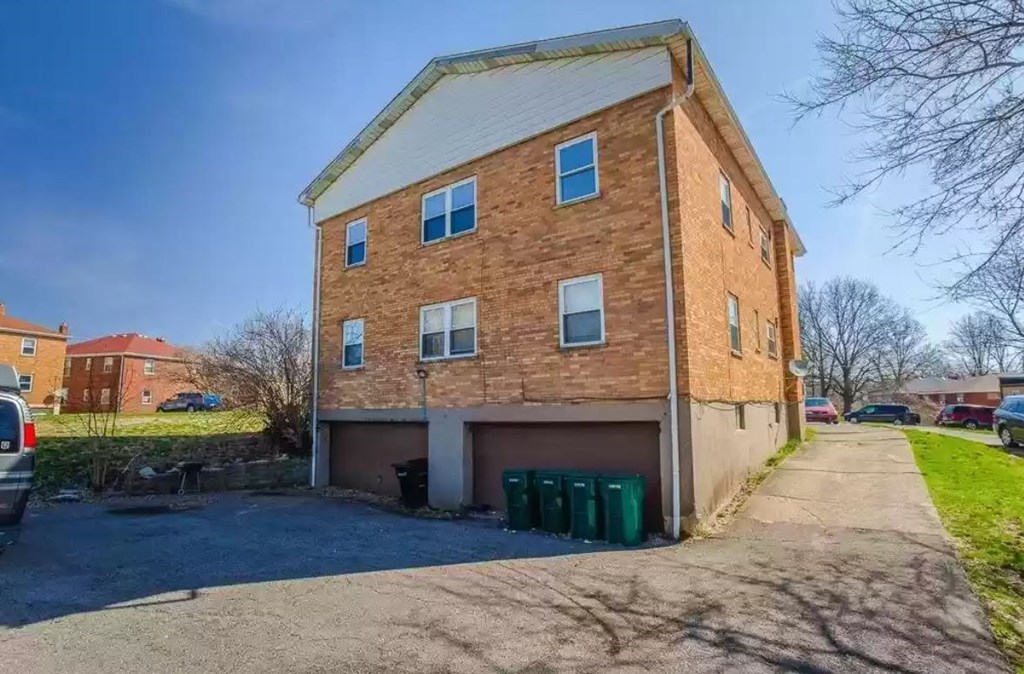 a brick apartment building with a driveway and garbage cans
