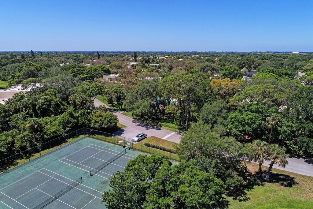 an aerial view of a tennis court with trees and a parking lot