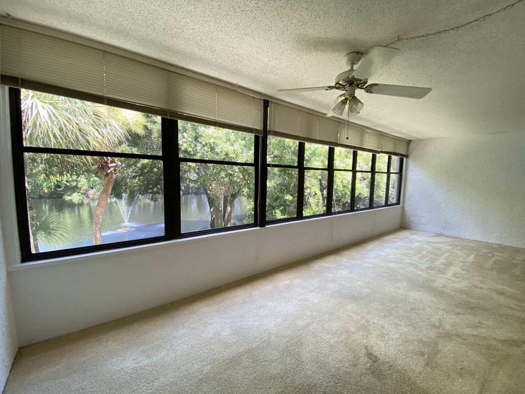 an empty living room with large windows and a ceiling fan