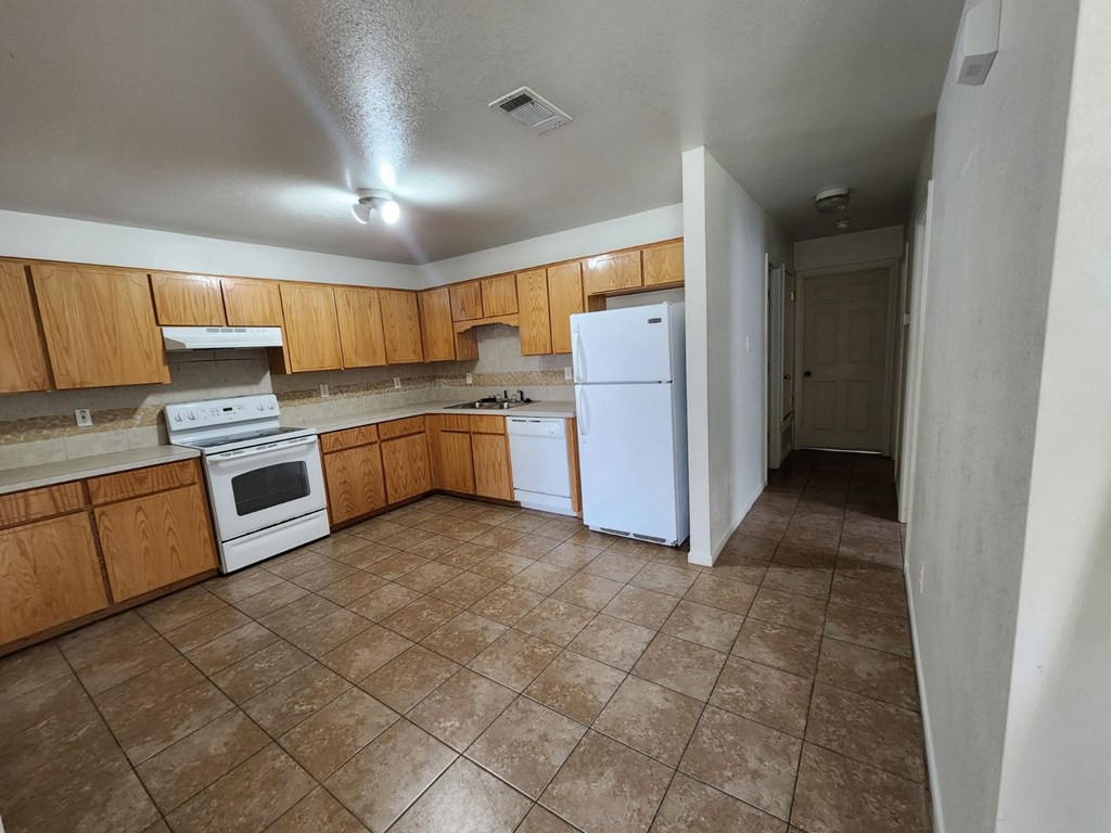 an empty kitchen with white appliances and wooden cabinets