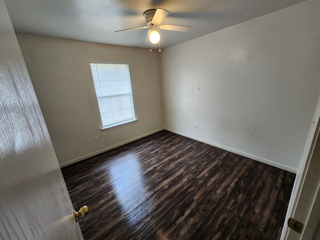 an empty living room with wood flooring and a ceiling fan