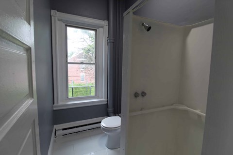 A bathroom with a toilet, a window, and a shower.