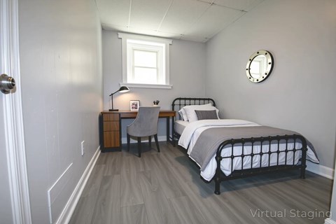 A bedroom with a bed, desk, chair, and window.