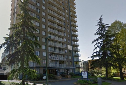 A tall residential building with balconies and a sign in front.