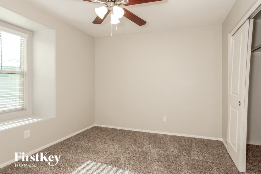 the spacious bedroom has a ceiling fan and carpeted flooring