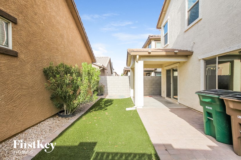 a backyard with a green lawn and a house with a garbage can