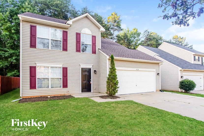 a beige house with red shutters and a lawn