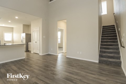 A spacious living room with wood flooring and a staircase on the right.