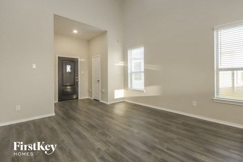 A spacious room with wood flooring and a window with blinds.