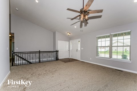an empty living room with a ceiling fan and a staircase