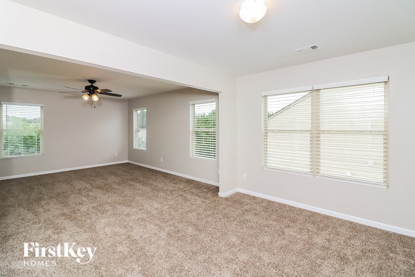 A room with a carpeted floor, a ceiling fan, and two windows with blinds.