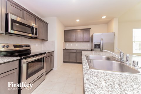 A kitchen with a stove top oven, microwave, refrigerator, and sink.