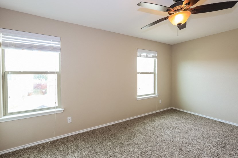 A room with a ceiling fan and two windows.