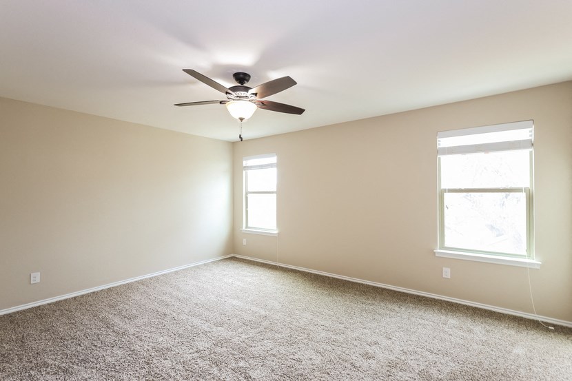A room with a ceiling fan and two windows.