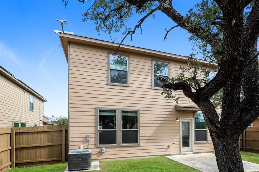 A house with a tan siding and a tree in front.