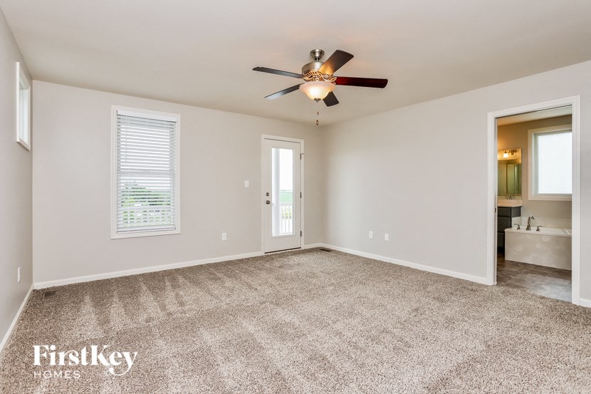 an empty living room with a ceiling fan and a door to a bathroom