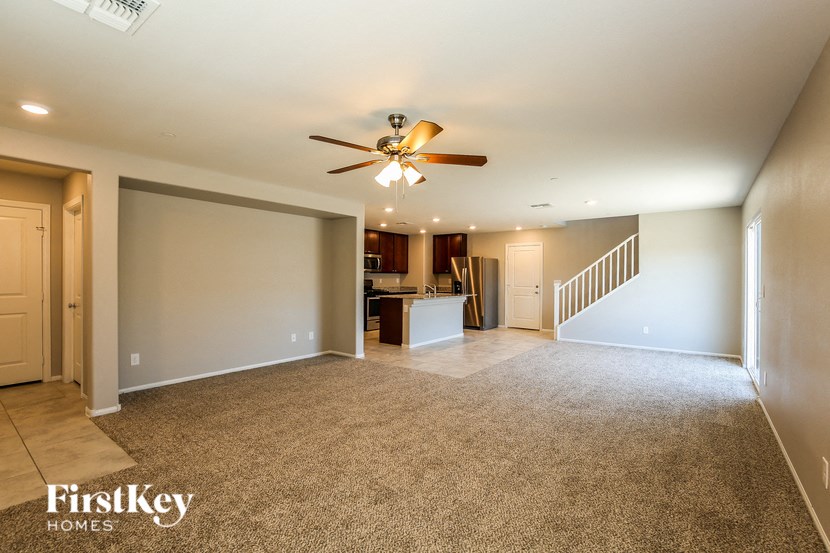 an empty living room with a ceiling fan and a kitchen