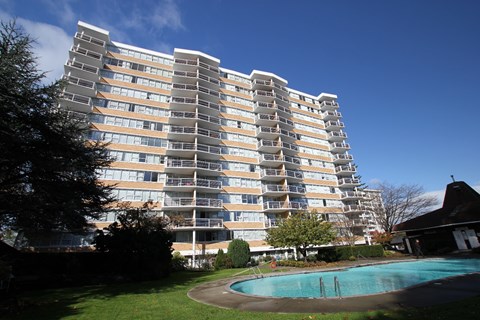 A tall residential building with a swimming pool in front.