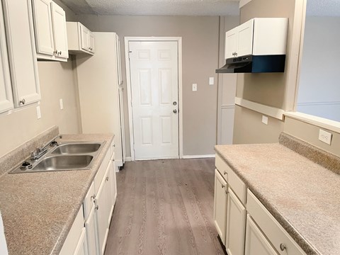 A kitchen with a sink, cabinets, and a door.