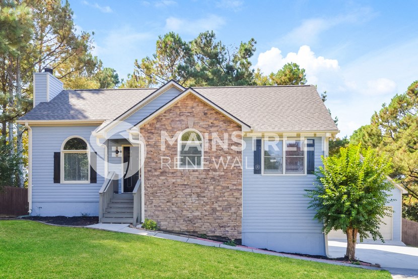 front view of a small white house with a lawn and trees
