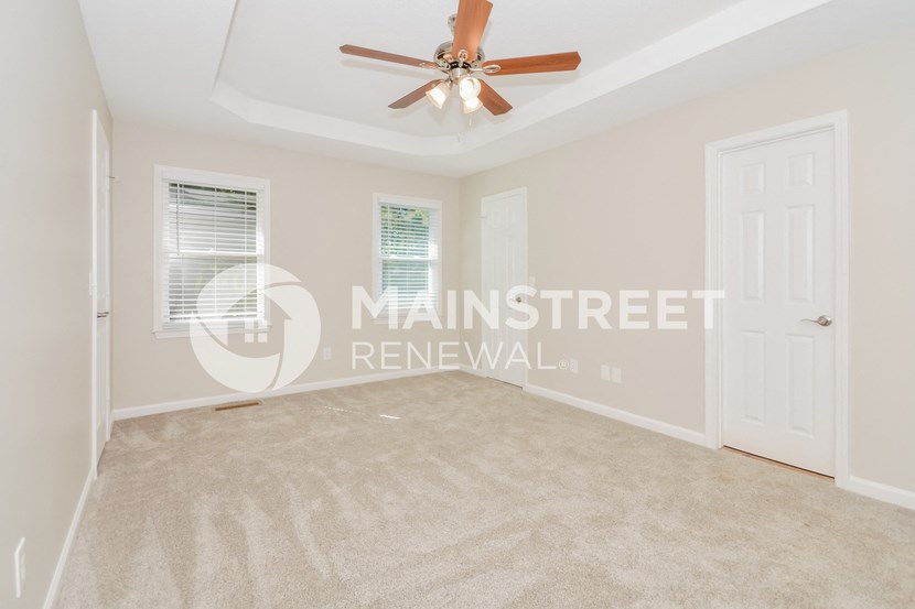 a bedroom with beige carpet and a white door and a ceiling fan