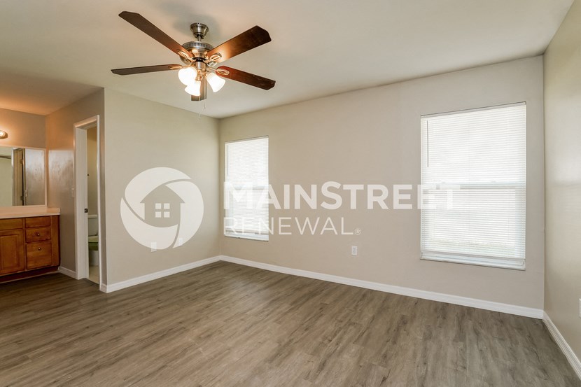 an empty living room with a ceiling fan and a door to a bathroom