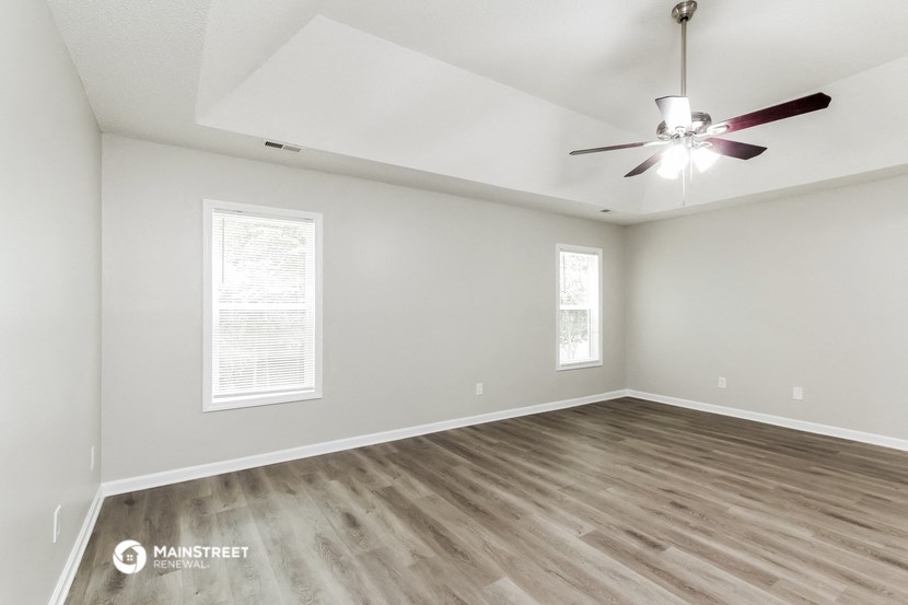 the spacious living room with hardwood floors and a ceiling fan