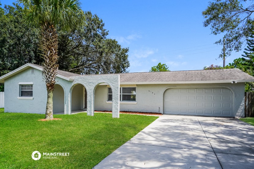 a white house with a driveway and a palm tree