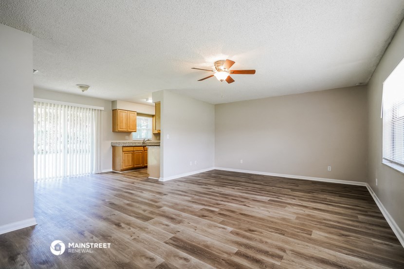 an empty living room with a ceiling fan and a kitchen