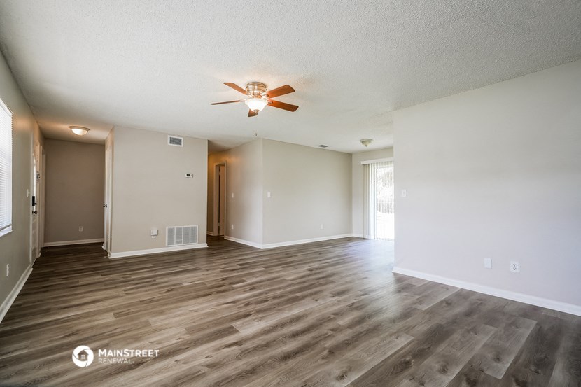 the spacious living room with wood flooring and a ceiling fan