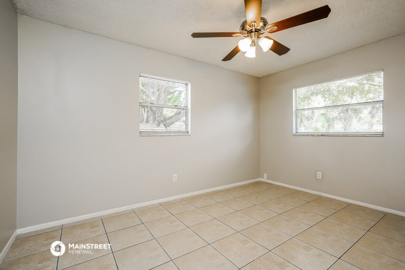 the spacious living room has a ceiling fan and tiled floors