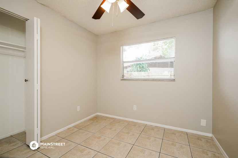 the living room of an empty home with a window and a ceiling fan