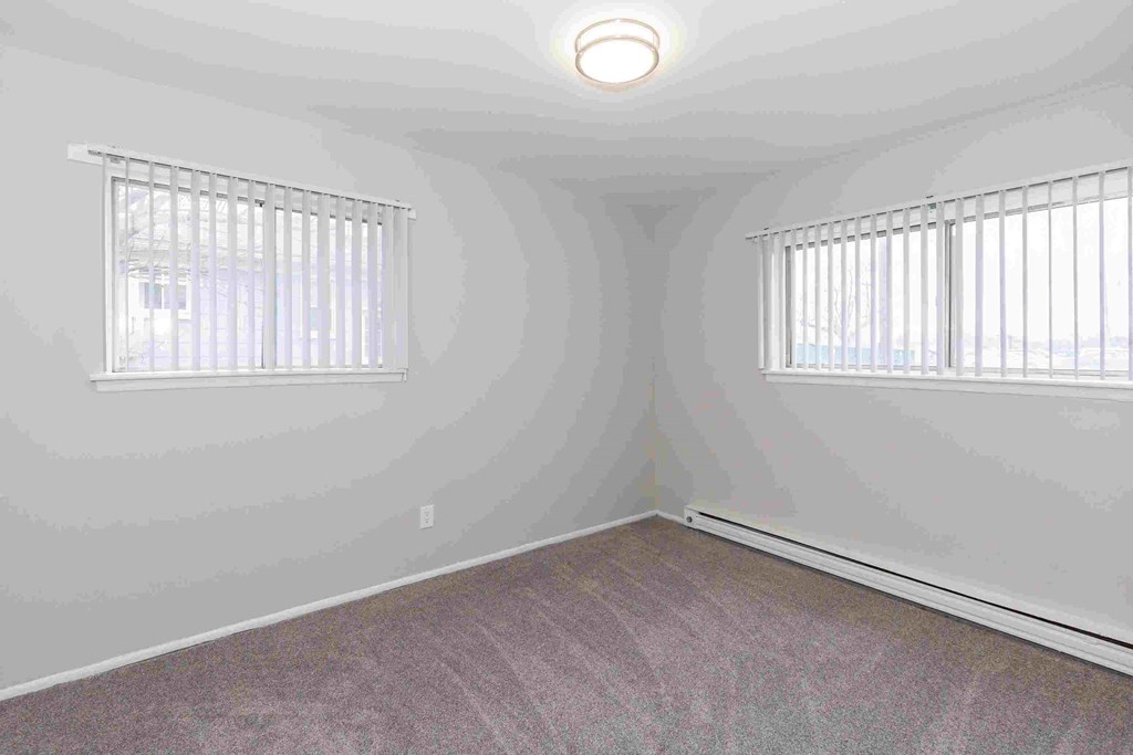 an empty room with two windows and a carpet
