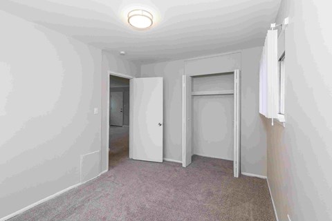 a bedroom with white walls and carpet and a door to a closet