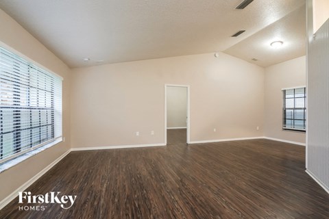 A spacious room with wooden flooring and a large window with blinds.