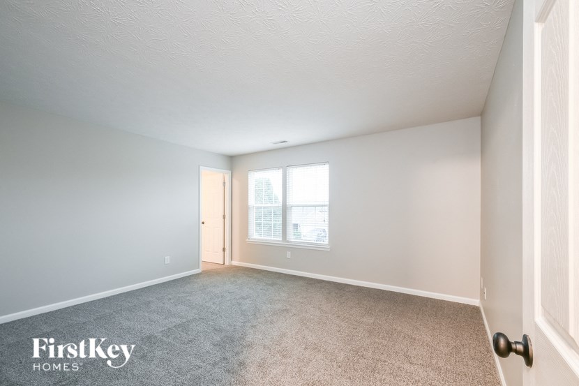 a spacious living room with carpet and a door to a bedroom