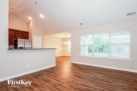 A spacious room with wooden floors and a kitchen area with a refrigerator and cabinets.
