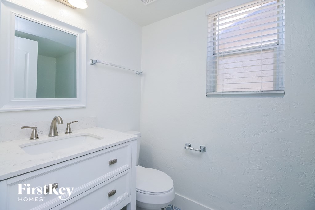 A white bathroom with a toilet, sink, mirror, and window.