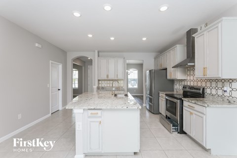 A kitchen with white cabinets and a marble island.
