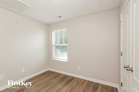 a bedroom with white walls and wood flooring and a window