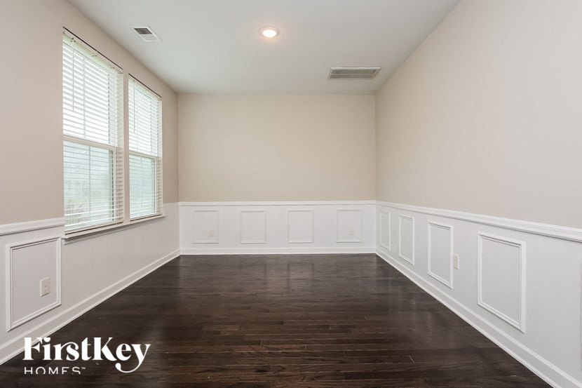 A room with wooden floors and white walls, with a window on the left side.